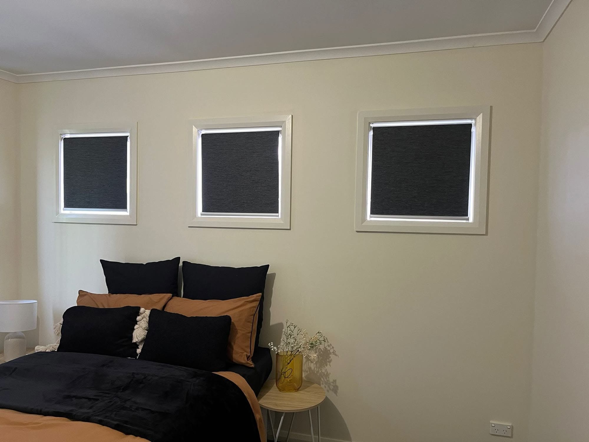 Three blockout roller blinds above a bedroom bed