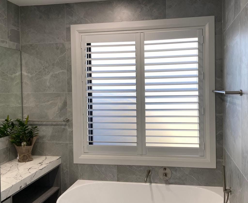 Plantation shutters above a bath in a grey ensuite