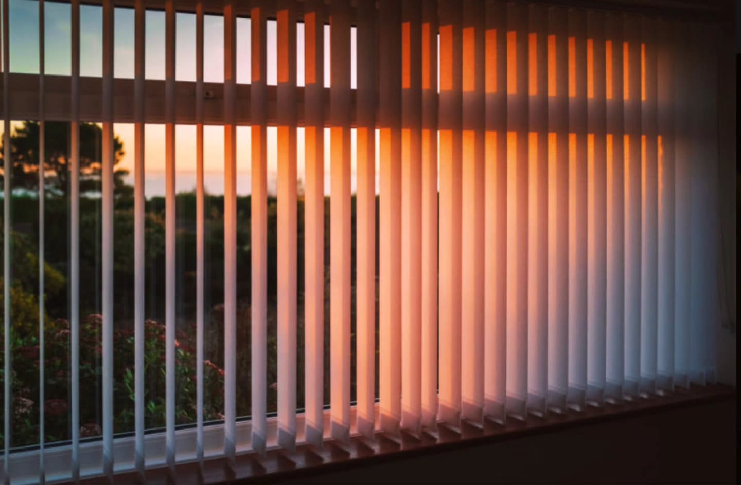 Vertical blinds catching a sunset over the garden
